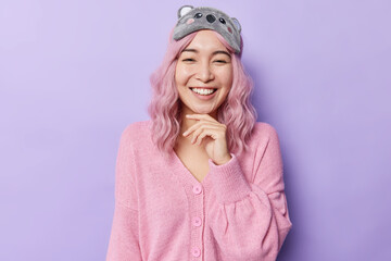 Portrait of cheerful young Asian woman with pink hair keeps hand under chin smiles happily has good...