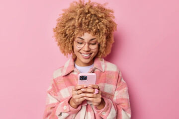 Glad fashionable woman dressed in checkered jacket browses internet on modern device sends text...