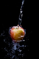 plenty of water is poured over an apple against a black background