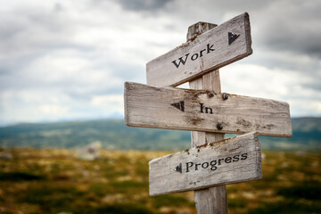 work in progress text quote written in wooden signpost outdoors in nature. Moody theme feeling.