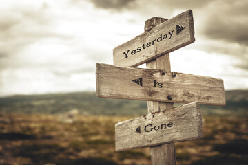 yesterday is gone text quote written in wooden signpost outdoors in nature. Moody theme feeling.