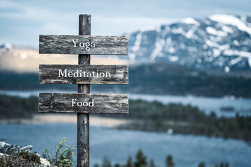 yoga meditation food text quote written on wooden signpost outdoors in nature with lake and mountain scenery in the background. Moody feeling.