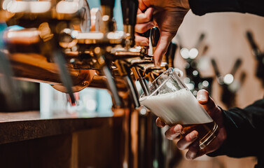 bartender's hands pour craft beer from a tap into a glass in bar