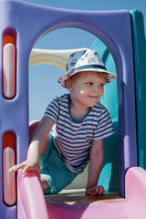 A little boy in a hat and a striped sailor shirt, go through through an arch on a beach playground.