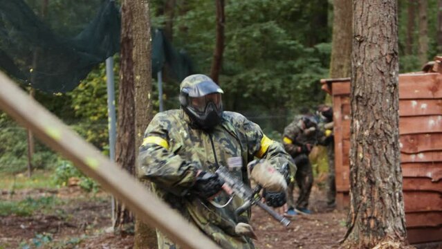 Paintball team in uniform and masks, extreme sport. Paintball player in mask and camouflage aiming by a paintball gun. Paintball team, battle on playground in the forest.