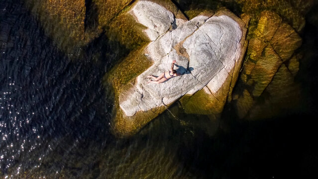  girl sunbathes on a stone island in the middle of a lake in Karelia, Russia.