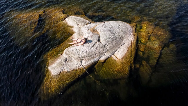  girl sunbathes on a stone island in the middle of a lake in Karelia, Russia.