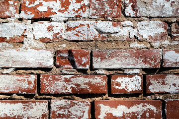 Old brickwork covered with peeling plaster, brick and cement at the joints between the bricks