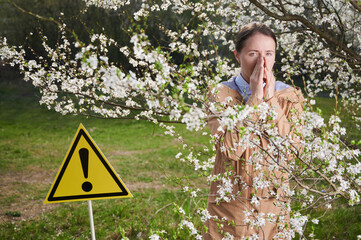 Woman allergic suffering from seasonal allergy at spring, posing in blossoming garden at...