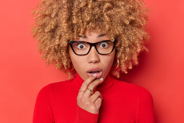 Headshot of shocked woman gazes scared at camera keeps hand on lips looks with amazement cannot...