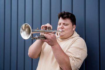Obraz premium Young street musician playing the trumpet near the big blue wall
