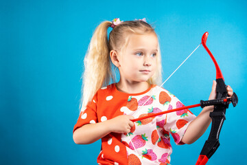 A beautiful little girl in a red dress shoots a bow. The concept of children's games, striving for...