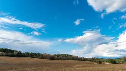 cloud movement over an agricultural field. A spring landscape with a forest, an empty field and clouds. The plowed field is ready for planting grain crops.