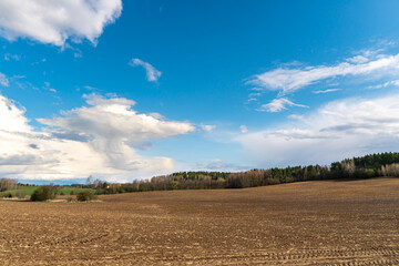 cloud movement over an agricultural field. A spring landscape with a forest, an empty field and clouds. The plowed field is ready for planting grain crops.