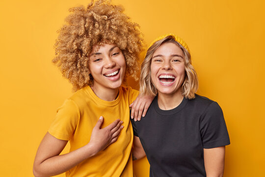 Best Female Friends Laugh Happily Feel Amused Smile Broadly Have Fun Together Dressed In Casual T Shirts Isolated Over Vivid Yellow Studio Background. Positive Human Emotions And Feelings Concept