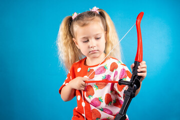 A beautiful neat girl in a red dress shoots a bow. The concept of children's games, striving for a...