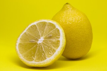 Przekrojona cytryna z opartą o nią całą cytryną na żółtym tle