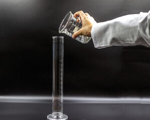 The woman hand held the beaker and filled the graduated flask. Isolated graduated flask. Black background.