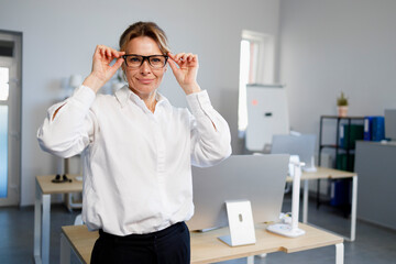 Portrait of cute mature female office worker in glasses and white shirt