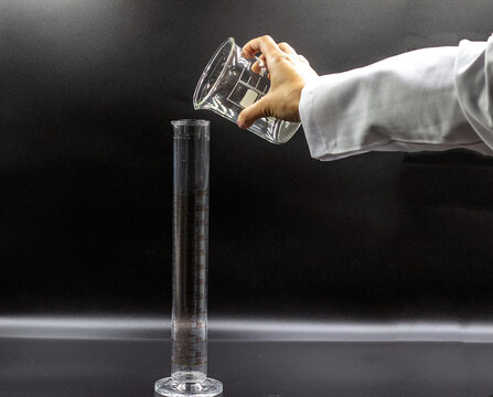 The woman hand held the beaker and filled the graduated flask. Isolated graduated flask. Black background.
