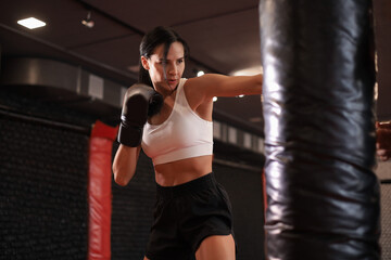 Young woman boxer athletic wearing gloves strikes punching bag during training preparation for...