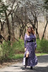 Uśmiechnięta kobieta w długiej wiosennej kwiecistej sukience na spacerze w parku wiosną