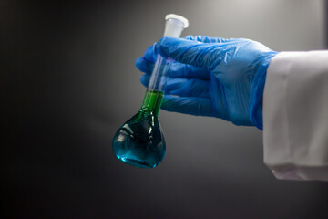 Researcher in the laboratory. Scientific concept.  The researcher held the volumetric flask with green liquid. Chemical test tubes for medical, pharmaceutical, and analytical. Hand with gloves. 