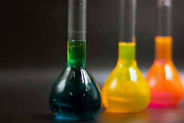 Close-up picture of colorful liquids in the volumetric flask. Chemical substances, and solutions in the black background. The colorful solutions line up on the black background. 