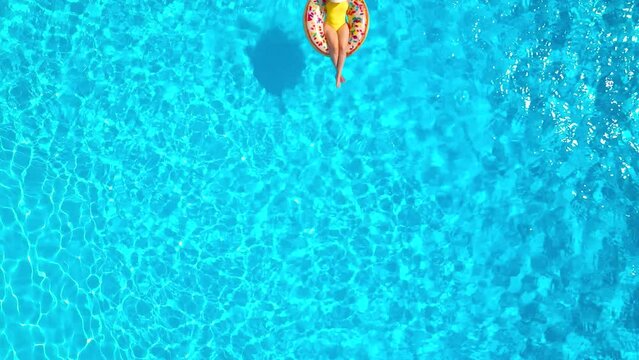 Aerial view of a woman in yellow swimsuit lying on a donut in the pool