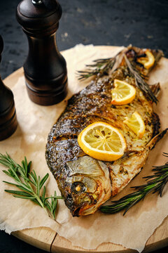 Baked fish in oven with lemon and rosemary laid out cutting board and parchment paper.On dark background with two straws.