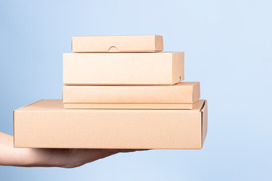Stack of cardboard boxes in female hands. Blank brown parcel boxes on light blue background. Packaging, shopping, free shipping, delivery concept