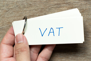 Man hold the flash card with handwriting word VAT (abbreviation of value added tax) on wood...