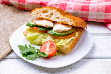 sandwich chicken breast and cucumbers and tomatoes on white plate
