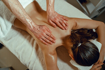 Fototapeta na wymiar Top view masseur man doing back massage using oil to a woman in spa salon. Therapy, resort