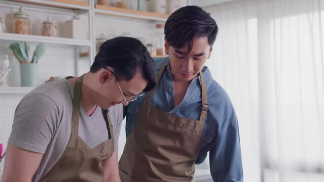 Asian gay couple tease each other very happy and romantic in their home kitchen while cooking together
