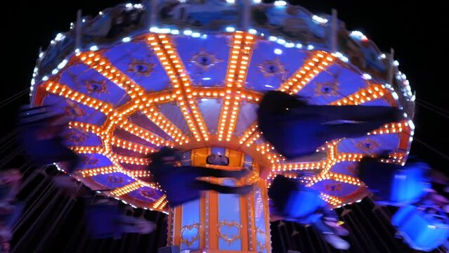 Night carousel on which visitors ride. Amusement park in the evening in colorful lights. Illuminated merry go round carousel