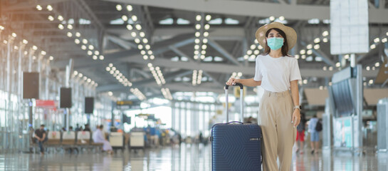 Young female wearing face mask with luggage walking in airport, protection Coronavirus disease...