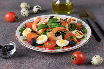 Salad with shrimps, quail eggs, arugula, cherry tomatoes and black olives on plate on brown background