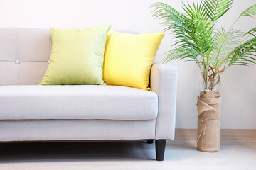 Part of gray sofa with green and yellow cushions and plant, interior design concept.