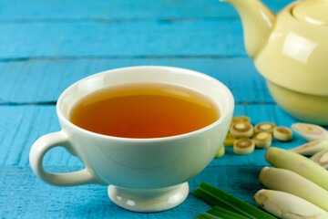 Cup of hot lemongrass tea with sliced and green leaf on blue wooden background. Lemongrass for healthy herbal drink concept.