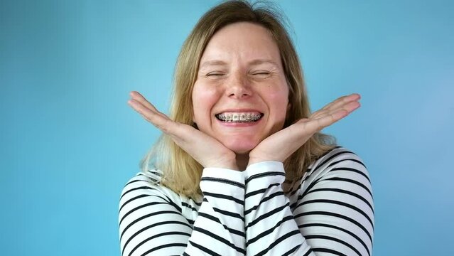 Young woman with dental braces laughing isolated on blue colour background. Studio. Cute lovely girl with metal braces on white clear teeth smiling in clinic. Close Up. Positive Emotion. Stomatology.