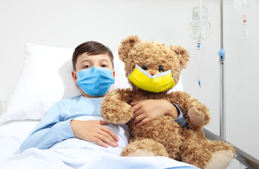 Humanitarian Aid, help for medical protection for Ukraine war, child in hospital bed with teddy bear wearing protective face mask yellow and blue colors of Ukraine flag. Injured Ukrainian refugees