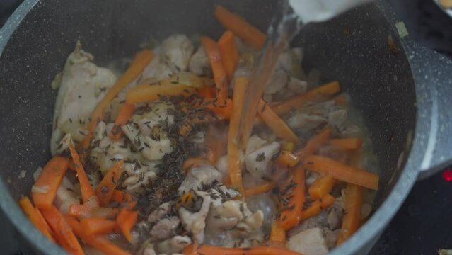 The cook pours water into the zirvak for pilaf. The process of cooking an Asian dish is pilaf.