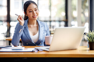 Fototapeta premium Asian Businesswoman Using laptop computer and working at office with calculator document on desk, doing planning analyzing the financial report, business plan investment, finance analysis concept.