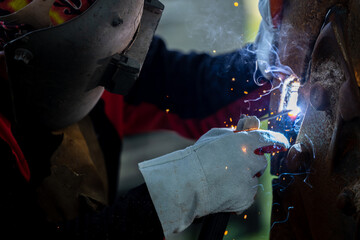 Welder in iron mask helmet welds with electric arc steel welding, Industrial worker at the factory...