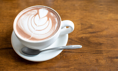 Morning in holiday time to relax with hot coffee and Latte art (Tulip pattern) in a white ceramic cup with stianless steel spoon on old wooden table background in coffee cafe ,Chill out day concept.