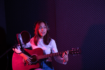 Asian female singer playing guitar and recording in the studio.