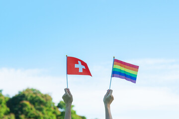 hands showing LGBTQ Rainbow and Switzerland flag on nature background. Support Lesbian, Gay, Bisexual, Transgender and Queer community and Pride month concept