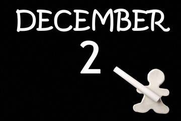 A small white plasticine man writing the date 2 December on a black board. Business concept. Education concept.