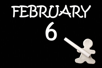 A small white plasticine man writing the date 6 February on a black board. Business concept. Education concept.